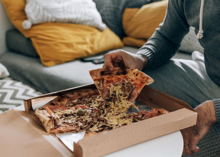 Man sitting on couch, eating pizza. pizza box, pizza delivery.