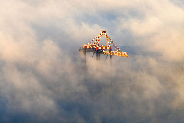 Tip of shipping crane surrounded by mist as sunsets