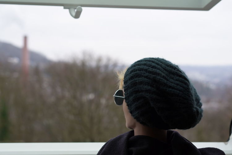 Rear view of woman standing at open window during winter