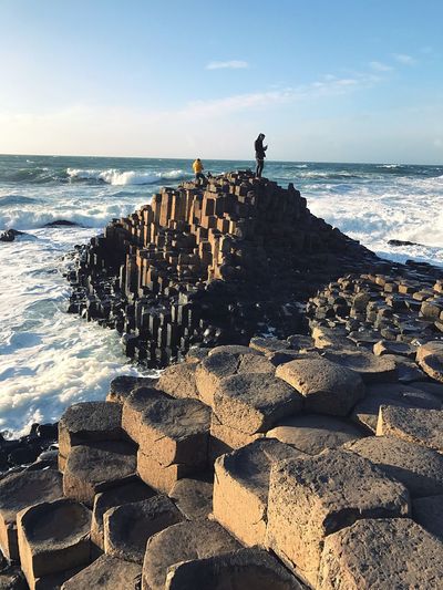 People standing on rock by sea against sky