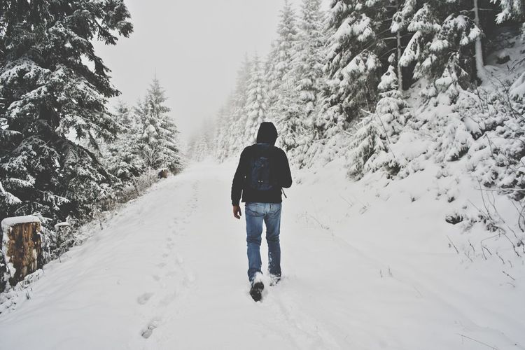 Rear view of man walking on snow covered field