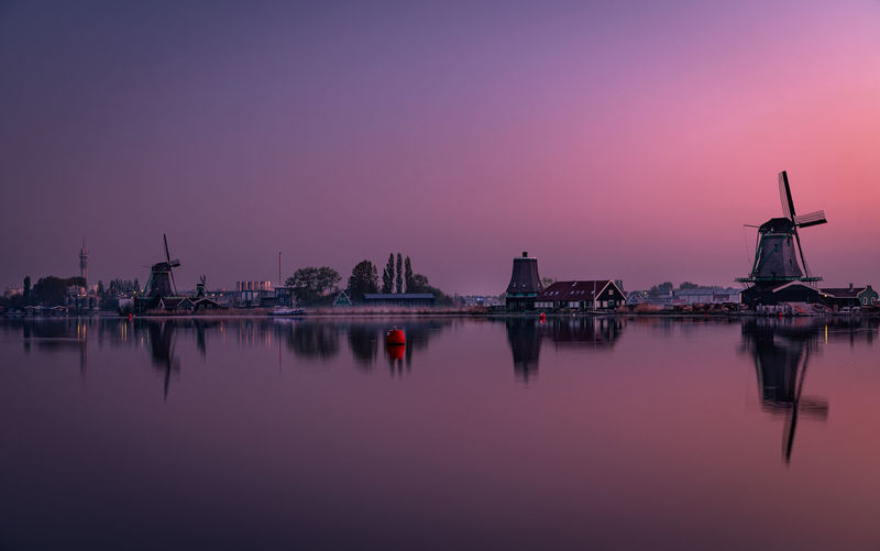 Traditional windmills by lake against clear sky during sunset
