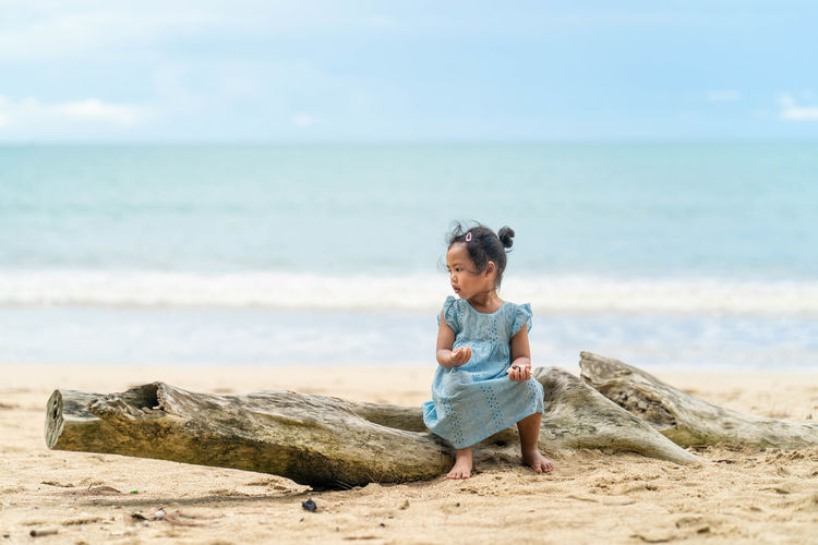 Girl sitting on sand at beach against sky