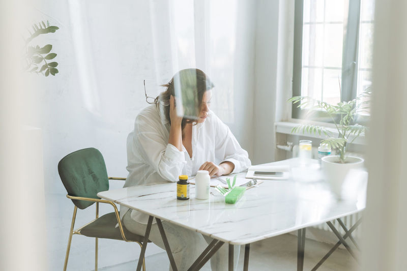 Thinking brunette woman doctor nutritionist plus size in white shirt working on table 