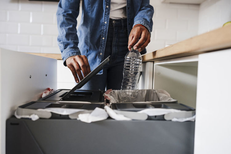 Young woman recycling plastic bottles in kitchen at home
