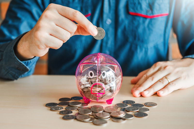Midsection of man putting coin in piggy bank
