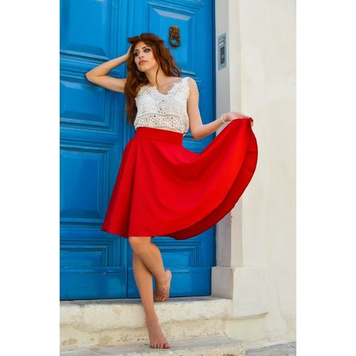Thoughtful young woman holding red skirt while standing by closed door