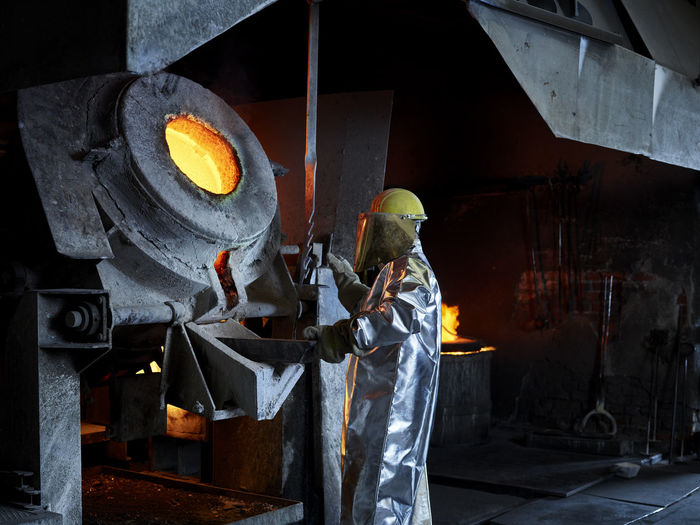 Blue-collar worker melting metal in furnace at industry