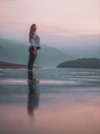 Woman standing in sea against sky during sunset