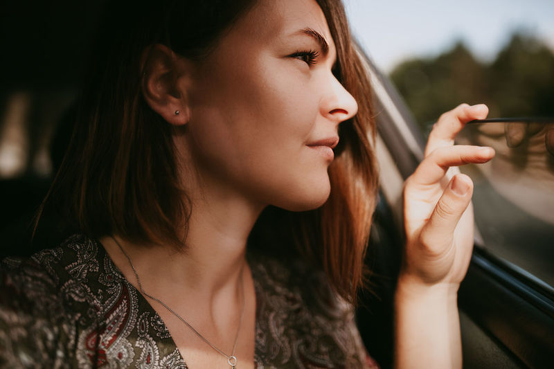 Young woman with dark short hair and silver earrings looks thoughtfully out the open car window