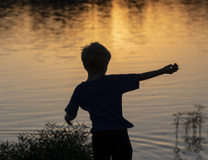 Rear view of boy standing in lake during sunset