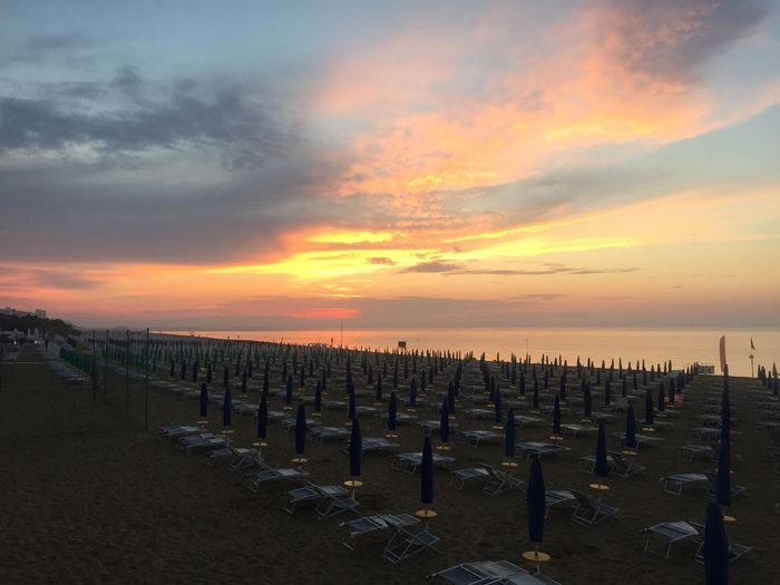 Long lines of beach chairs  at the sea against sky during sunrise 