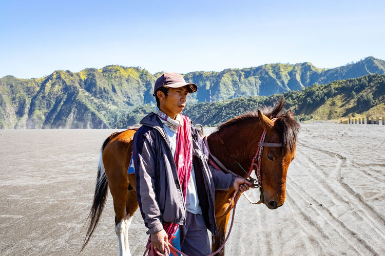 Man standing with horse on land against mountain range
