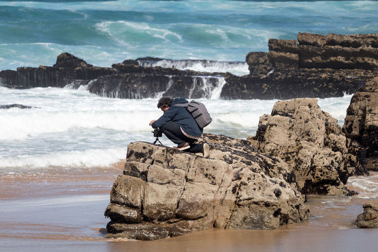 Side view of man photographing from rock at beach