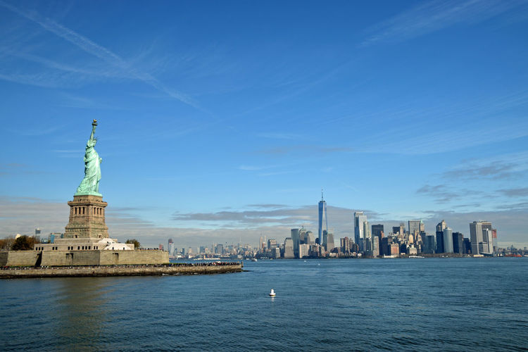 Statue of liberty by river in city against blue sky