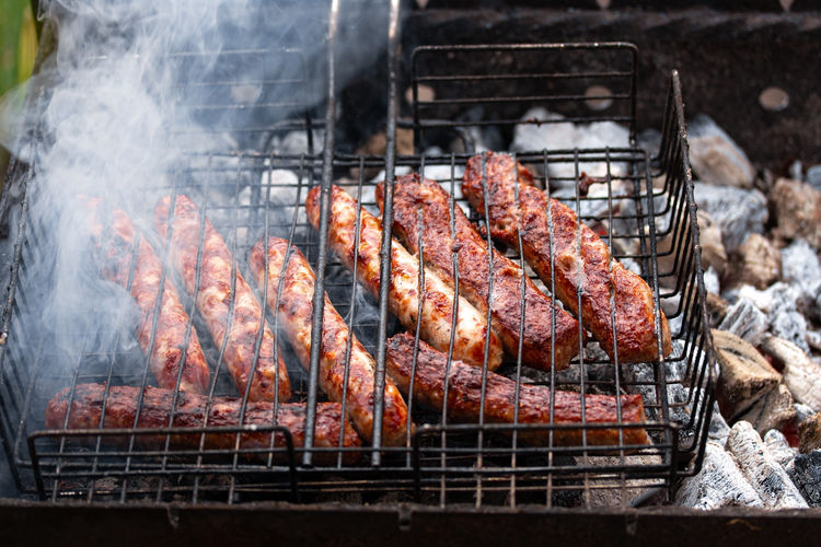 Appetizing crisp pork sausages on barbecue grill with smoke. summer outdoor picnic. 