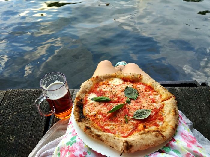 Low section of woman with pizza sitting on pier over lake