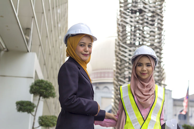 Low angle portrait of happy female architects standing against office building