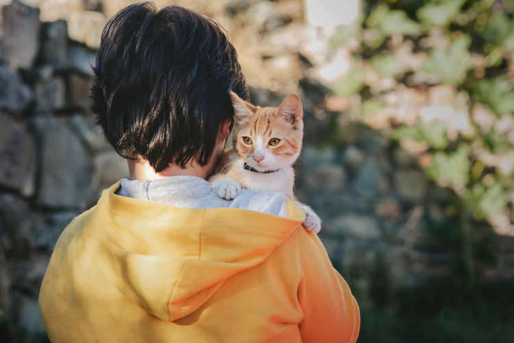Rear view of boy holding cat outdoors
