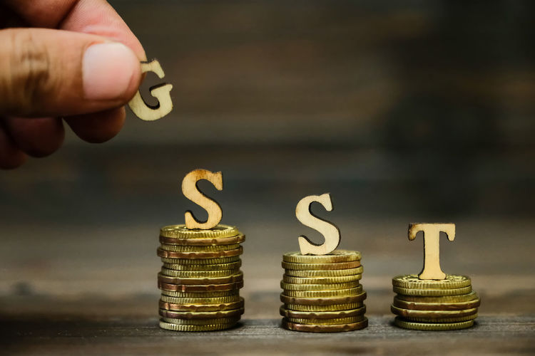 Cropped hand with gst text on stacked coins at table