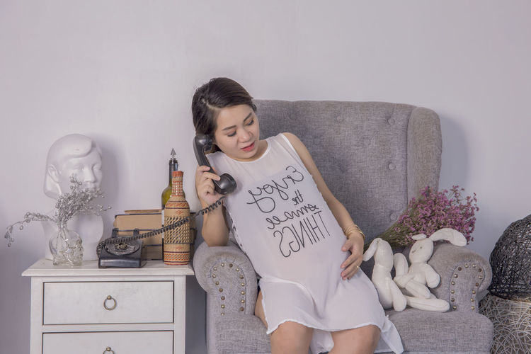 Pregnant woman talking on rotary phone while sitting at home