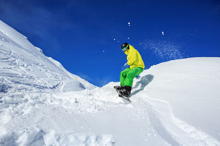Full length of man snowboarding on snowcapped mountain against sky