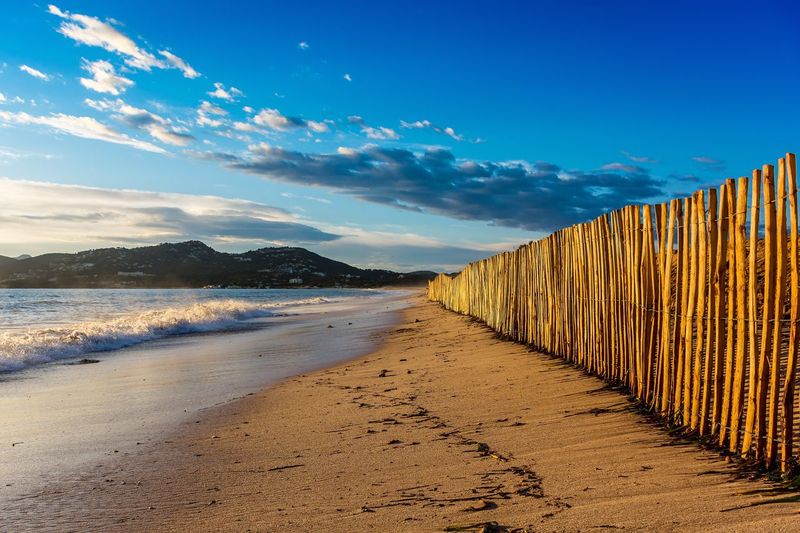 Wooden fence at beach against sky
