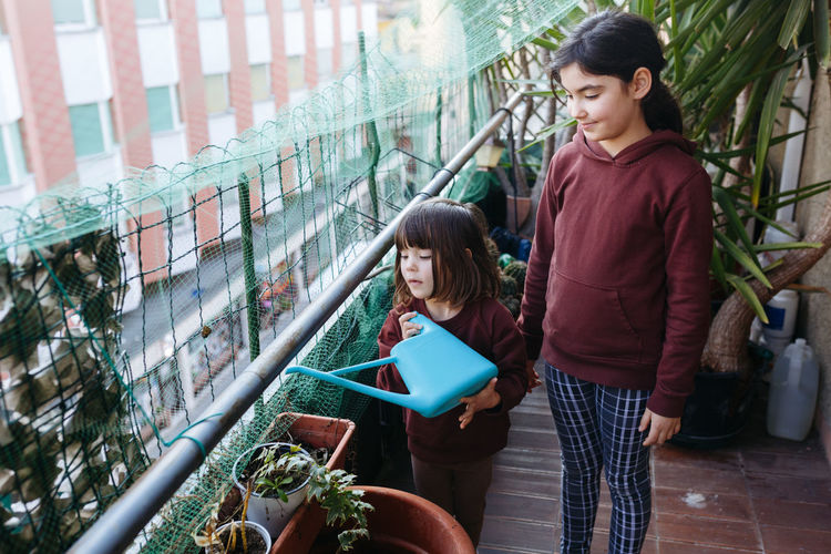 High angle view on two children on apartment balcony watering the plants