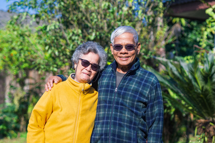 Portrait of elderly couple wearing sunglasses standing and smiling in garden.
