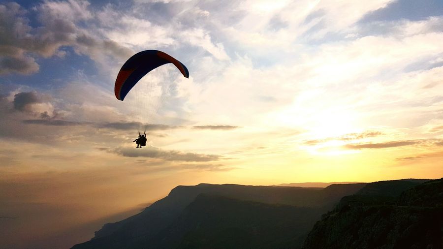 Silhouette people paragliding over mountains against orange sky