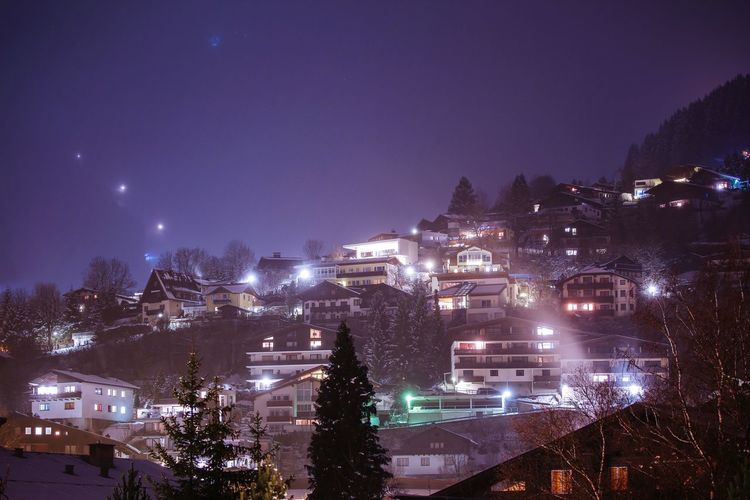 Night view of illuminated village houses on forest slopes of winter alps in austria