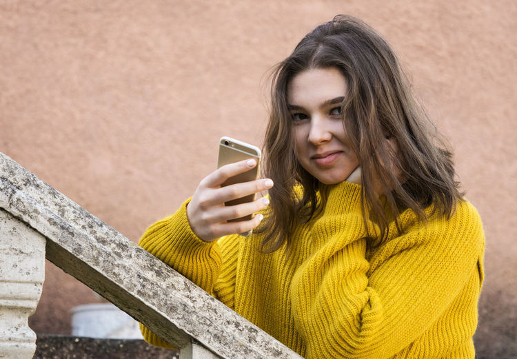 Teen girl in a yellow sweater with a smartphone