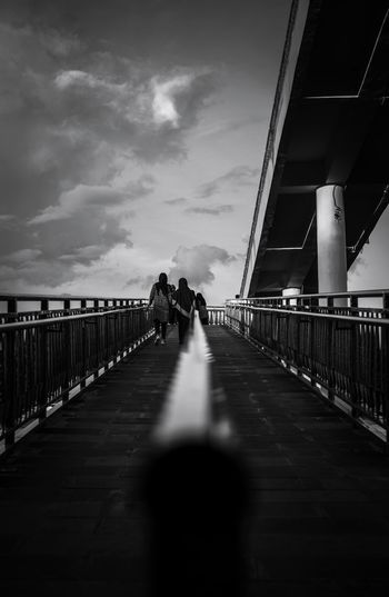 People walking on footbridge against sky