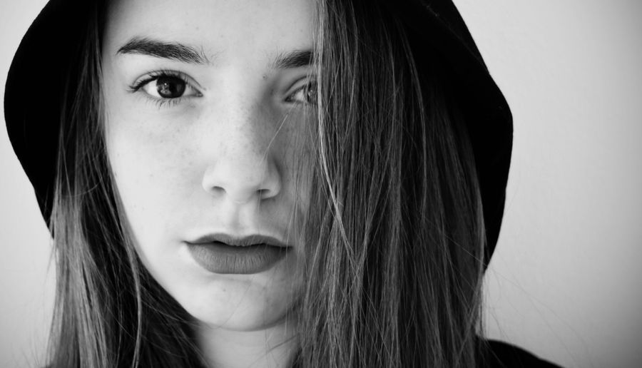 Close-up portrait of teenage girl wearing hat against wall