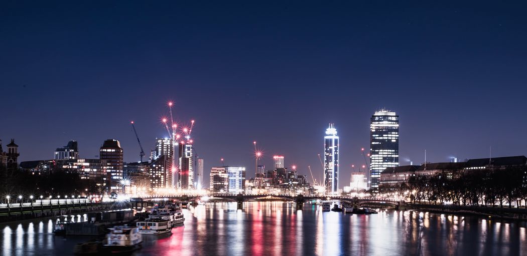 Illuminated buildings by river against sky at night