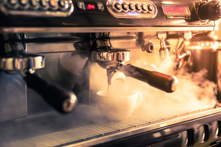 Close-up of machinery pouring coffee in cup at cafe