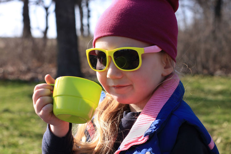 Smiling child in colorful clothes drinking tea from green reusable cup. eco-friendly family picnic.