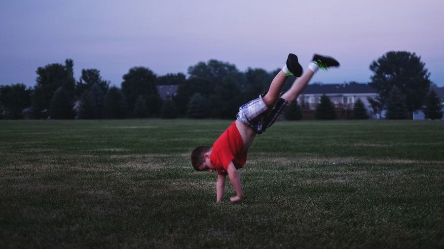 Full length of boy performing handstand on grassy field against sky