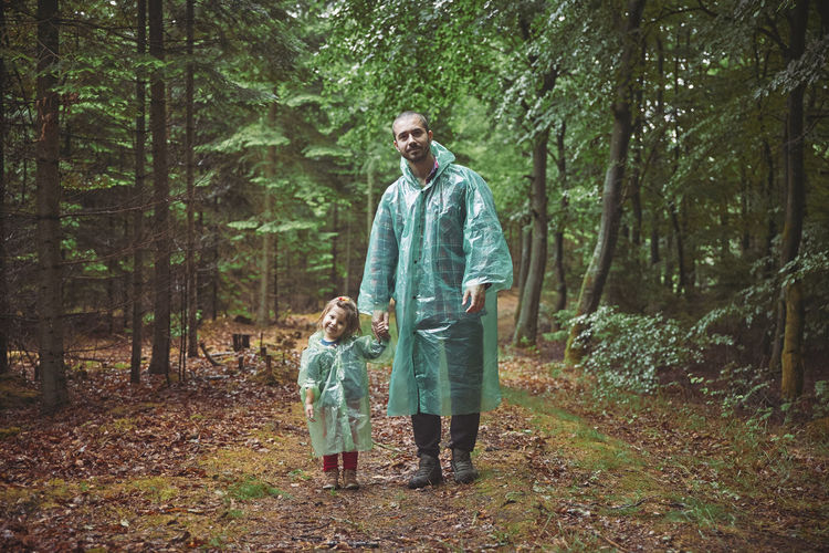 Father and daughter in raincoats walk in the evening forest