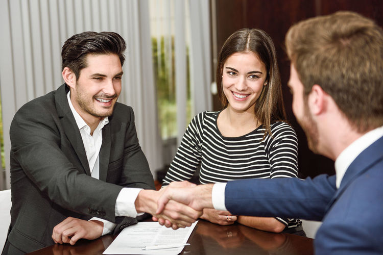 Smiling businessmen shaking hands by businesswoman
