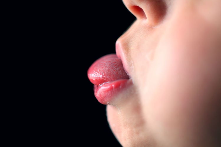 Cropped image of child sticking out tongue against black background