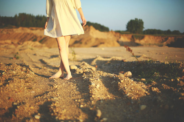 Low section of woman standing with crossed leg on dirt road