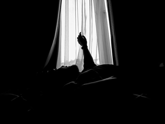 Silhouette man looking through window while lying on bed