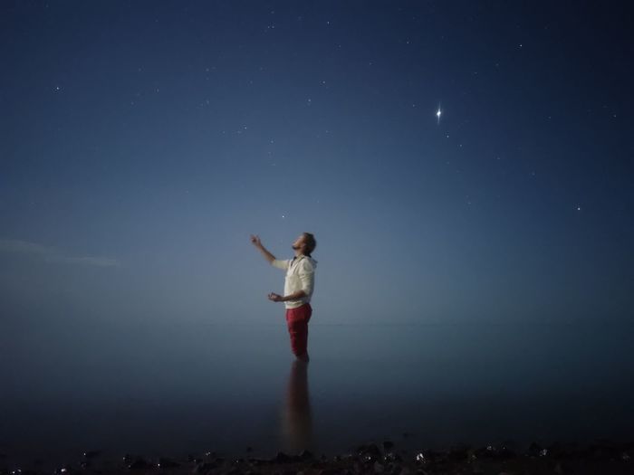 Man standing in sea against sky at night