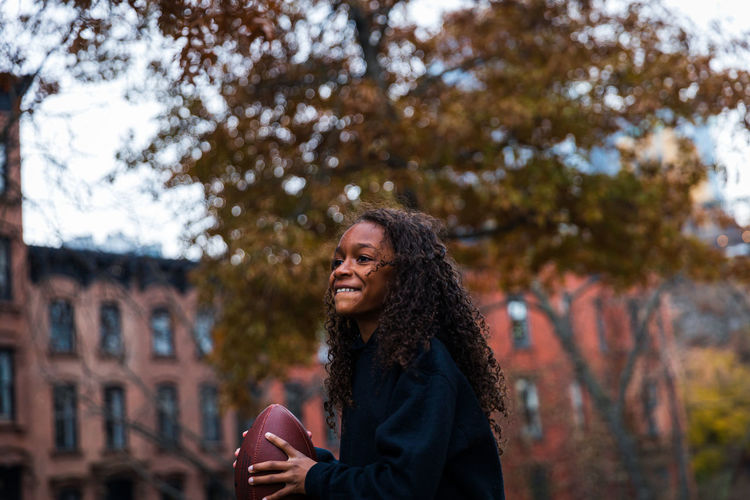 Smiling girl looking away while practicing american football in city