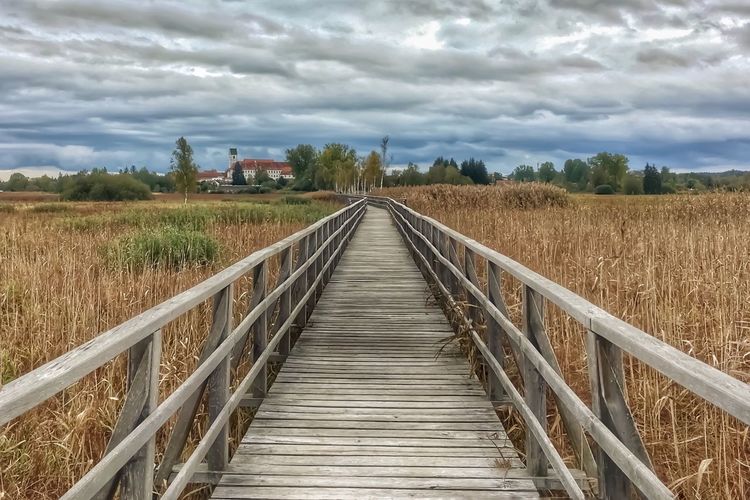 View of wooden footbridge on field against sky