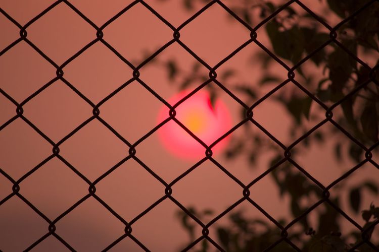 Full frame shot of chainlink fence against sky during sunset
