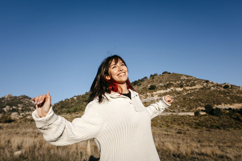 Smiling woman with arms outstretched on mountain