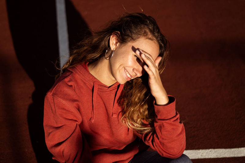 High angle view of young woman shielding eyes while sitting on sports track