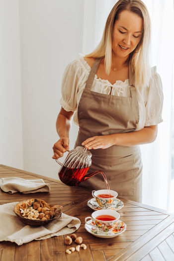 Blond woman in apron pouring hibiscus tea in cups on table